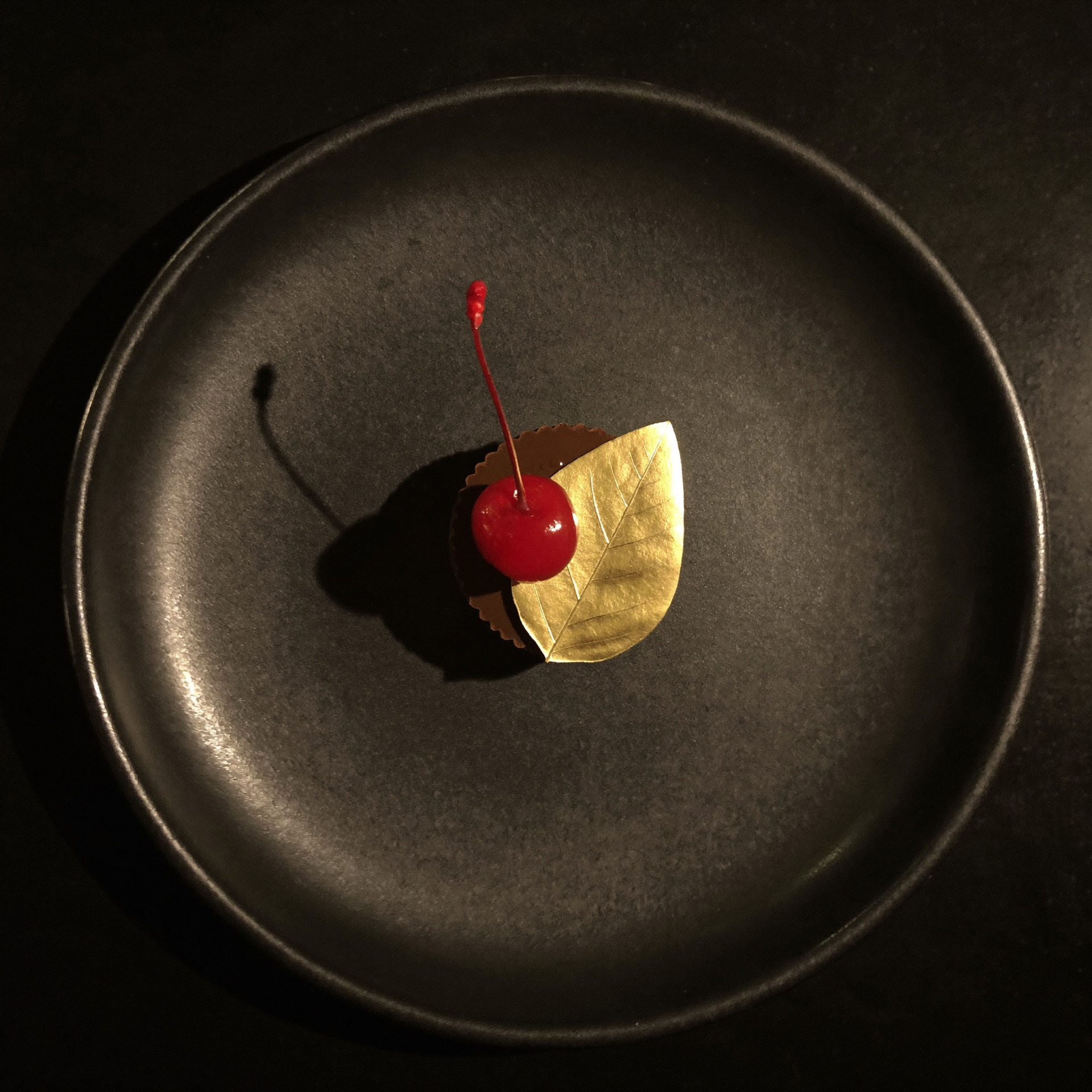 Schokoladentarte mit Kirsche und Blattgold auf schwarzem Teller